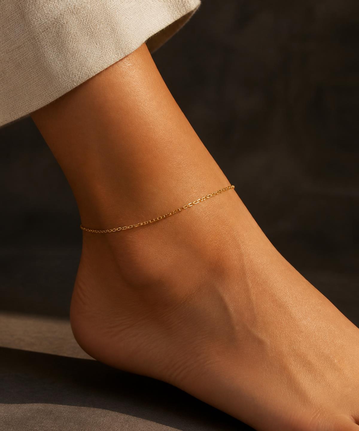 A fine gold-tone chain anklet worn on an ankle in warm afternoon light